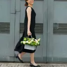 Woman in black dress carrying a basket of white and green flowers.
