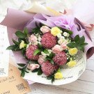Bouquet of pink and yellow flowers with greenery, wrapped in purple and white paper.