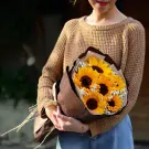A woman in a tan sweater holds a bouquet of sunflowers with baby's breath.