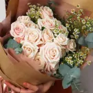 Bouquet of pale pink roses and daisies, wrapped in brown paper.