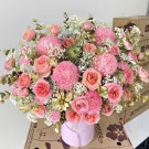 Pink peonies, roses, and carnations in a round pink box with gold accents.