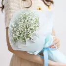 A woman holds a delicate bouquet of white baby's breath wrapped in light blue paper and tied with a blue ribbon.