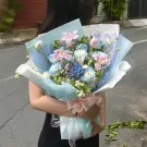 A woman holds a pastel pink and blue flower bouquet with roses, tulips, and succulents.