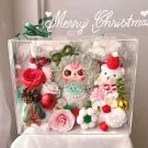 Clear box filled with plush toys, flowers, and Christmas decorations.