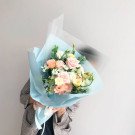 A pastel flower bouquet with roses, carnations, and eustoma, wrapped in light blue paper.
