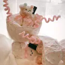 Plush teddy bears and pink paper roses in a decorative bouquet with piped pink trim.