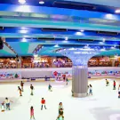 People ice skating at an indoor rink with blue and teal ceilings and decor.