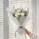 Elegant bouquet of white roses with delicate greenery, wrapped in white paper and tied with a gray ribbon.