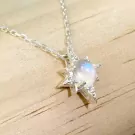 Star-shaped necklace with moonstone and diamonds on a wooden surface.