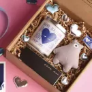Gift box with candle, plush bear, letter board, and heart embellishments on shredded paper.