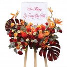 Floral arrangement for opening ceremony with red and orange roses, chrysanthemums, and tropical leaves.