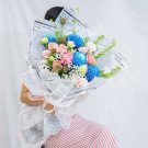 Bouquet of blue mums, pink roses, and other flowers wrapped in newspaper with a sheer white ribbon.