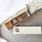 Box of four gourmet brownies with various toppings, next to a separate gift box.
