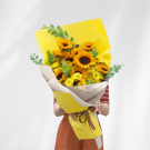 A bright yellow sunflower bouquet with baby's breath and eucalyptus, wrapped in yellow paper.