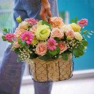 Pastel pink flower basket with roses, gerbera daisies, lisianthus, and carnations held by a person.