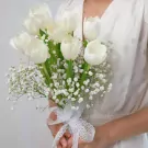 A bride holding a bouquet of white tulips and baby's breath, tied with a white lace ribbon.