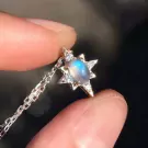 Star-shaped pendant necklace with moonstone and diamonds on a silver chain, held by fingers.