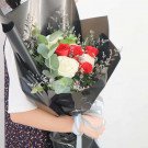Bouquet of red and white roses with eucalyptus and baby's breath, wrapped in black paper.