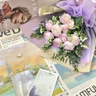 A bouquet of light purple and white roses on newspapers with fashion and travel images.
