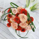 Pink roses and orange gerbera daisies arranged in a bouquet with green foliage.