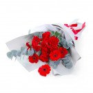 Bouquet of red gerberas and carnations with eucalyptus, wrapped in white paper and tied with red ribbon.