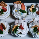 Six white mallow cupcakes topped with strawberries, marshmallows, and pretzels, one has a "Happy Woman's Day" tag.