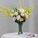 A clear glass vase holds a bouquet of yellow dancing lady orchids and pastel roses.