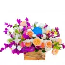 A wooden box overflowing with pastel purple, pink, and orange flowers, including roses, carnations, and orchids.
