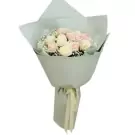 A bouquet of pink and white roses with baby's breath, wrapped in pale gray paper and tied with a cream ribbon.