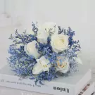 White roses and blue filler flowers arranged in a bridal bouquet on top of books.