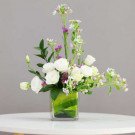 White lisianthus with purple and blue accents in a square glass vase.