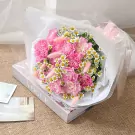 Pink carnation bouquet with daisies and bunny tails, wrapped in white and clear paper, resting on a Vogue book.