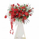 Grand red floral arrangement with roses and anthuriums on a white stand with red ribbons.