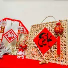 Tet gift basket with candy, fortune cat, red decorations, and a calligraphy banner.