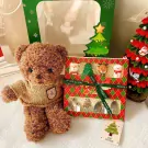Brown teddy bear in a sweater next to a Christmas gift box with Santa, reindeer, snowman, and tree decorations.