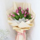 Pink and purple tulips wrapped in cream paper, tied with pink ribbon.