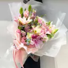 Pink lily bouquet with delphinium and star flowers, wrapped in sheer paper and tied with ribbon.