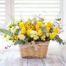 Basket of yellow roses, sunflowers, and carnations with eucalyptus greenery.