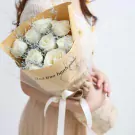 Bouquet of white roses with greenery, wrapped in brown paper and tied with a white ribbon.