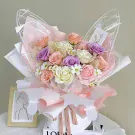 A bouquet of pastel roses and daisies wrapped in sheer pink and white paper with butterfly wing accents.