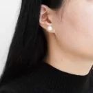 Close-up of a woman's ear wearing a single pearl stud earring.