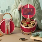 Red woven gift basket with bamboo handle, holding jars of treats and tea, featuring a horse design lid.