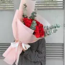 Bouquet of red roses and eucalyptus, wrapped in pink paper with a white ribbon.