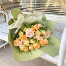 Bouquet of pink and peach roses with white accent flowers, wrapped in green paper.