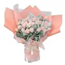 Pink and white roses with grey foliage wrapped in peach paper, tied with a white bow.