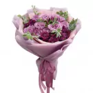 Bouquet of purple roses, chrysanthemums, and greenery wrapped in pale pink paper with a pink ribbon.