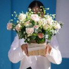 Coral pink roses, white daisies, and eucalyptus in a wooden box with fabric wrap.