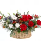 Basket of red roses, cotton, pine cones, and berries, decorated with greenery and thistles.