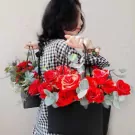 Woman carrying two black bags filled with red roses and greenery.