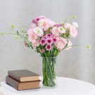 Pink and purple flowers in a glass vase with books on a table.